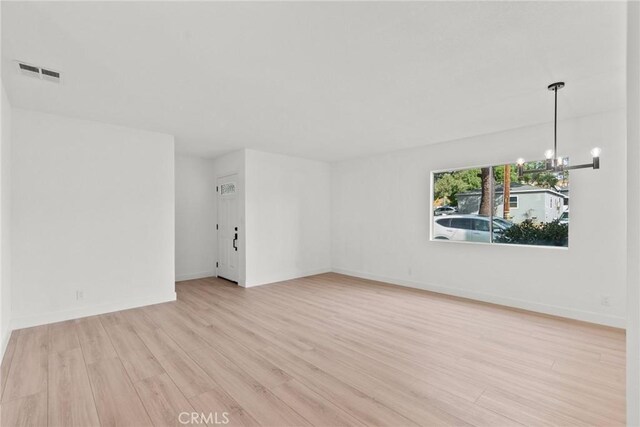 empty room with an inviting chandelier and light hardwood / wood-style flooring