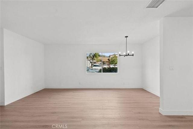 empty room featuring an inviting chandelier and light hardwood / wood-style floors