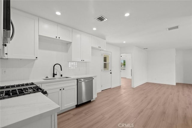 kitchen with sink, appliances with stainless steel finishes, white cabinetry, light stone counters, and tasteful backsplash