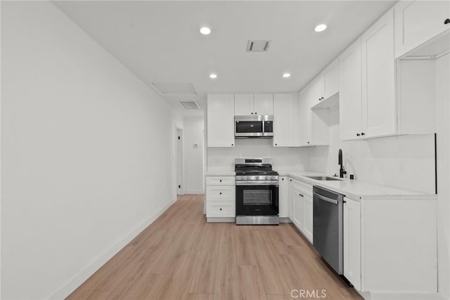 kitchen with light wood-type flooring, stainless steel appliances, sink, and white cabinets