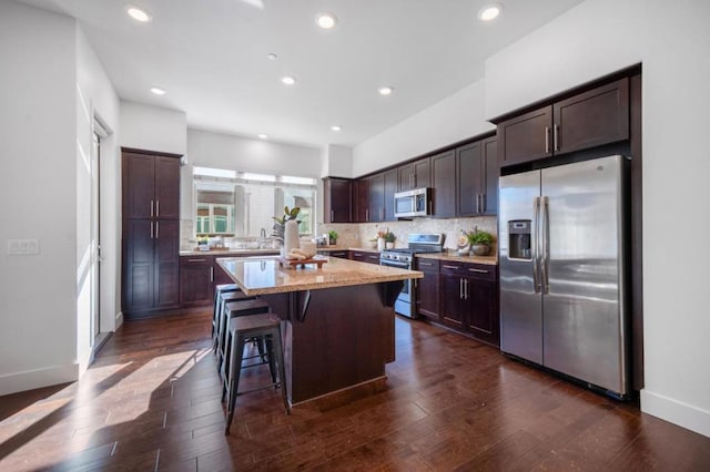 kitchen featuring a breakfast bar area, appliances with stainless steel finishes, backsplash, dark brown cabinets, and a center island