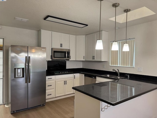 kitchen featuring appliances with stainless steel finishes, white cabinetry, sink, hanging light fixtures, and kitchen peninsula