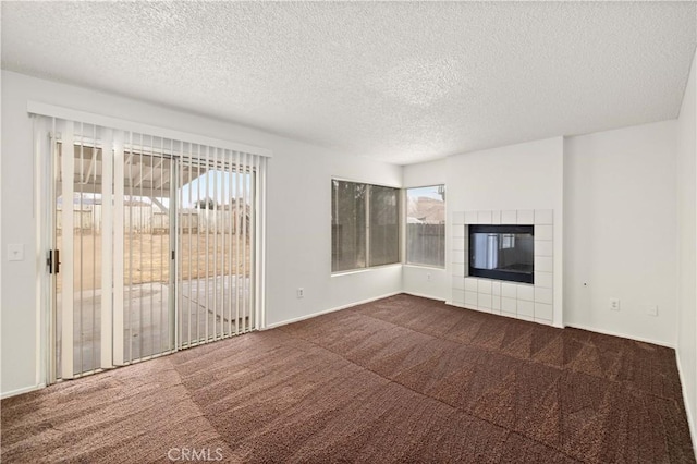 unfurnished living room with a tile fireplace, plenty of natural light, a textured ceiling, and dark carpet