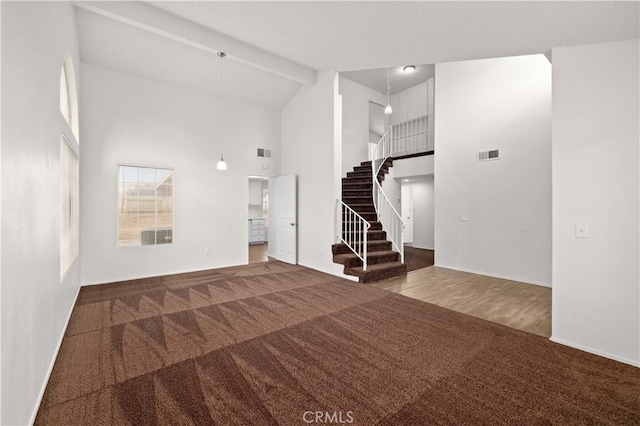 unfurnished living room featuring beamed ceiling, high vaulted ceiling, and carpet