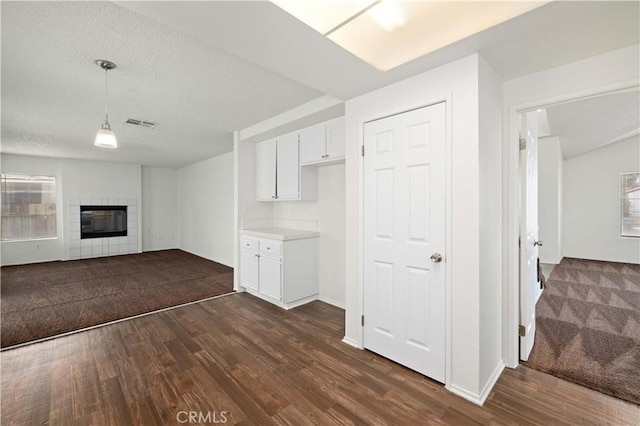 unfurnished living room featuring dark wood-type flooring, a tiled fireplace, and a textured ceiling