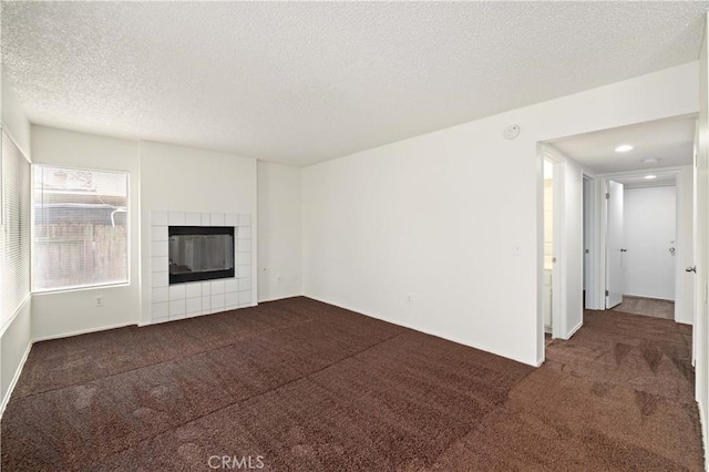 unfurnished living room with a fireplace, dark carpet, and a textured ceiling