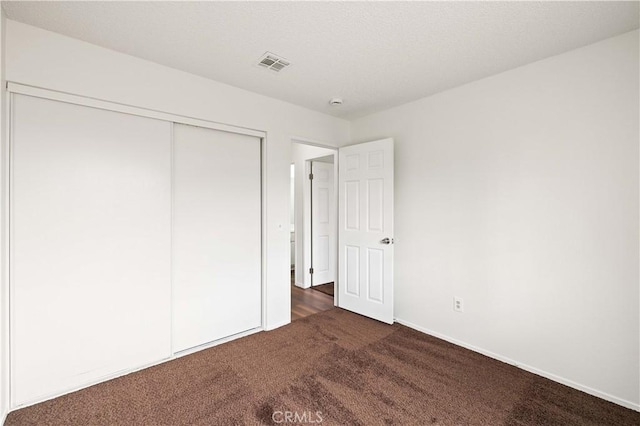 unfurnished bedroom featuring dark carpet and a closet