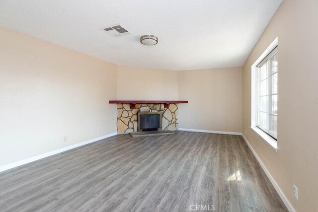 unfurnished living room featuring wood-type flooring and a stone fireplace