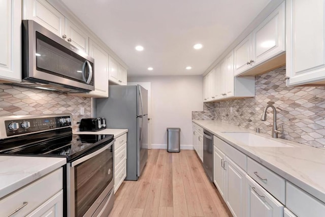 kitchen featuring white cabinetry, stainless steel appliances, light stone countertops, and sink