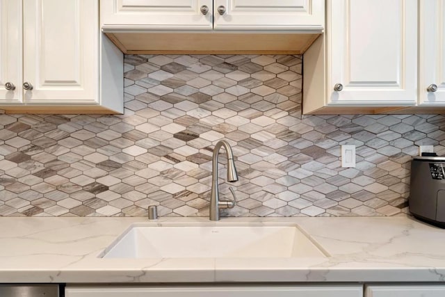 kitchen with backsplash, light stone countertops, sink, and white cabinets