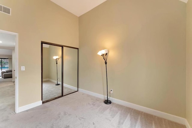 unfurnished bedroom with light carpet, high vaulted ceiling, and a closet