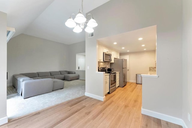 interior space featuring vaulted ceiling, appliances with stainless steel finishes, pendant lighting, white cabinetry, and light hardwood / wood-style floors