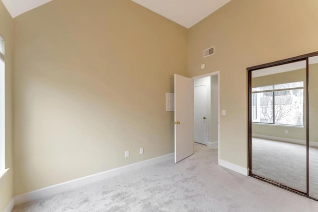 unfurnished bedroom featuring light carpet, high vaulted ceiling, and a closet