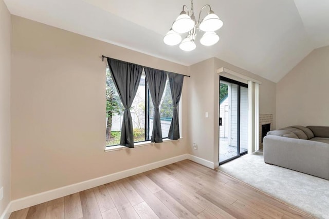 interior space with an inviting chandelier, a fireplace, vaulted ceiling, and light wood-type flooring