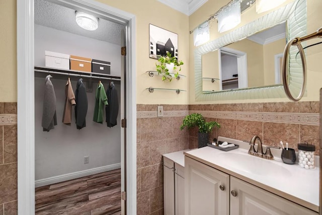 bathroom with wood-type flooring, a textured ceiling, tile walls, ornamental molding, and vanity