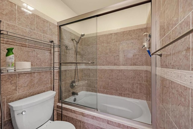 bathroom featuring bath / shower combo with glass door, toilet, and tile walls