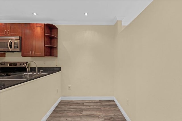 kitchen with sink, light hardwood / wood-style flooring, dark stone counters, ornamental molding, and stainless steel appliances