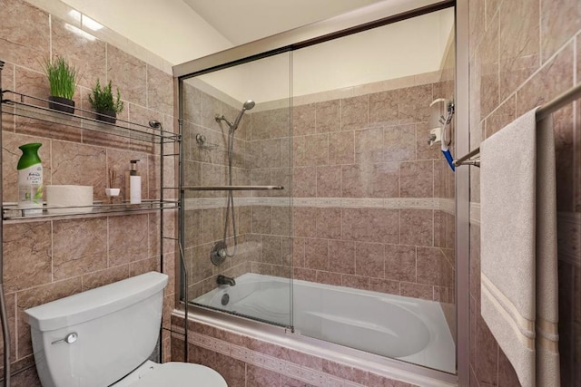 bathroom with tile walls, enclosed tub / shower combo, and toilet