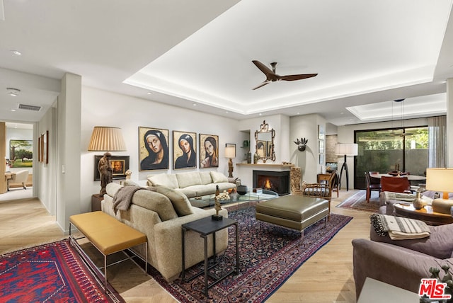 living room featuring ceiling fan, a tray ceiling, and light wood-type flooring