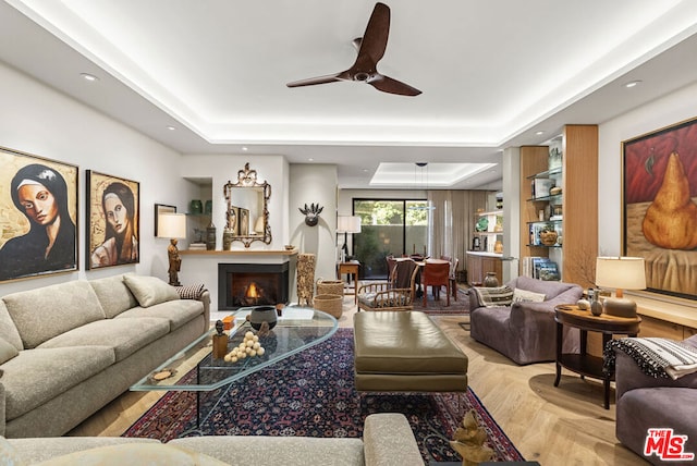 living room with ceiling fan, a tray ceiling, and light parquet floors