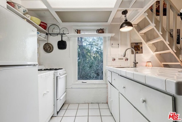 kitchen featuring sink, white cabinets, hanging light fixtures, tile counters, and white appliances