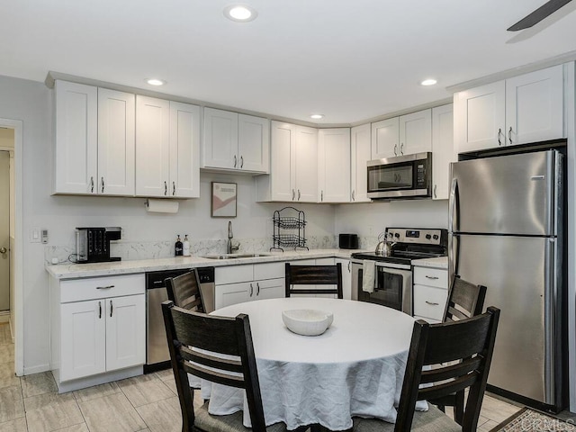 kitchen with white cabinetry, sink, light stone countertops, and appliances with stainless steel finishes