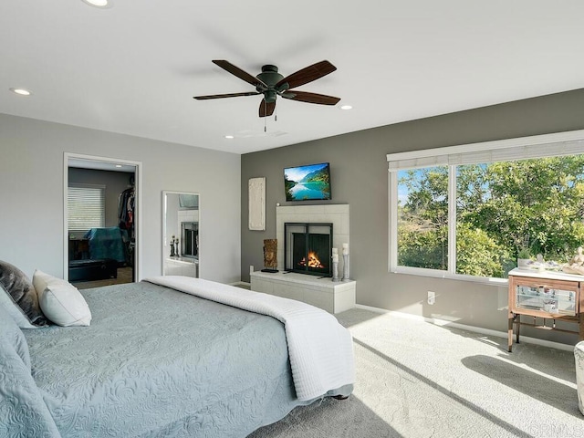 carpeted bedroom with a tiled fireplace, a walk in closet, and ceiling fan