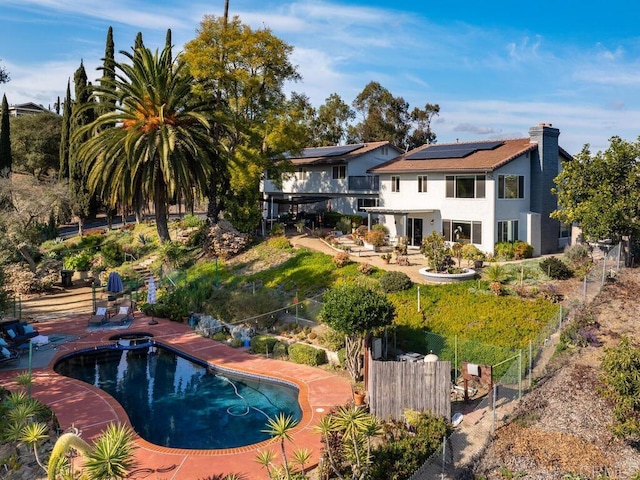 rear view of property with a fenced in pool, a patio area, and solar panels