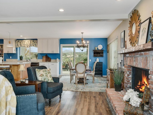 living room featuring hardwood / wood-style flooring, beamed ceiling, a brick fireplace, and a notable chandelier