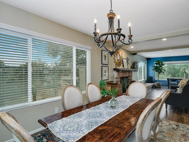 dining room with beam ceiling, a brick fireplace, hardwood / wood-style flooring, and a notable chandelier