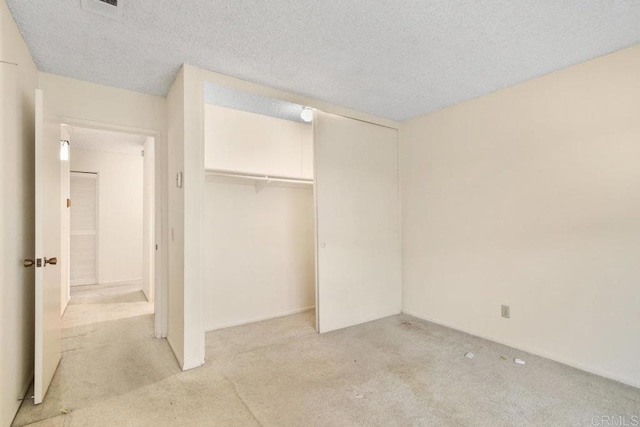 unfurnished bedroom featuring light carpet, a closet, and a textured ceiling