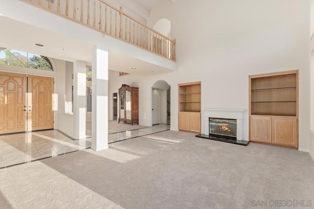 unfurnished living room with a towering ceiling, light carpet, and built in features