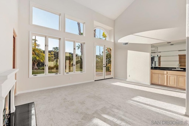 unfurnished living room with high vaulted ceiling, light colored carpet, and sink