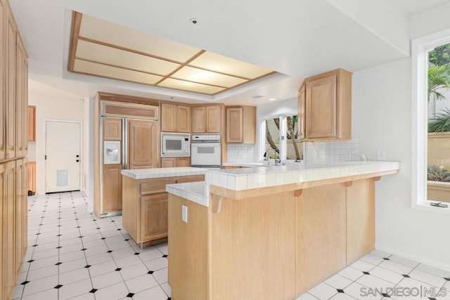 kitchen featuring built in appliances, tile counters, a kitchen breakfast bar, and kitchen peninsula