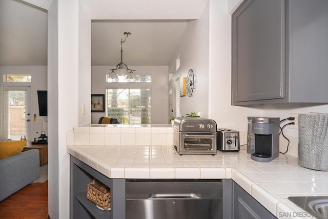 kitchen with pendant lighting, gray cabinetry, tile counters, wood-type flooring, and a chandelier