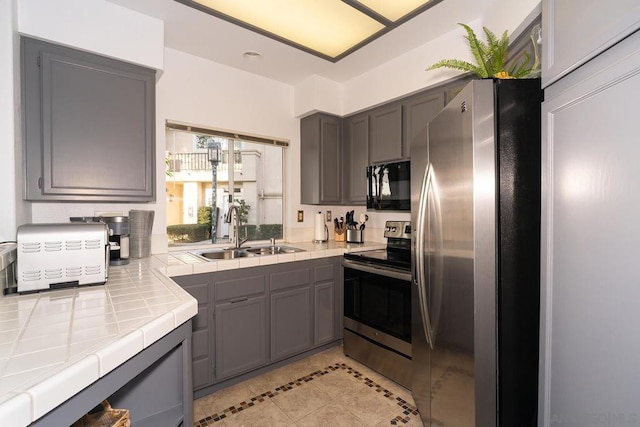 kitchen with sink, gray cabinetry, tile countertops, light tile patterned floors, and appliances with stainless steel finishes