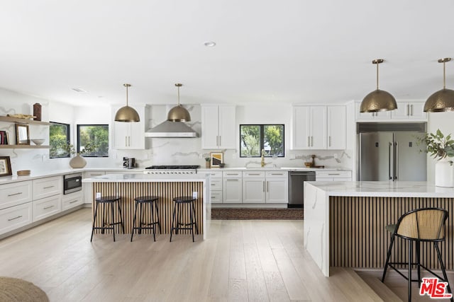 kitchen with a breakfast bar, a center island, appliances with stainless steel finishes, pendant lighting, and wall chimney range hood