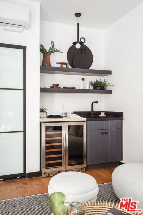 bar featuring beverage cooler, sink, a wall unit AC, and light hardwood / wood-style flooring