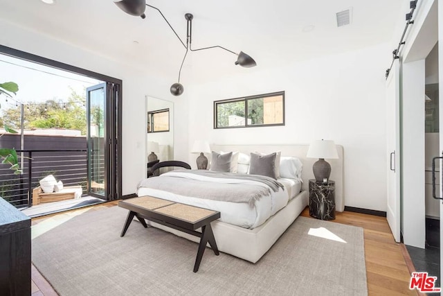 bedroom featuring a barn door, access to outside, and light hardwood / wood-style floors