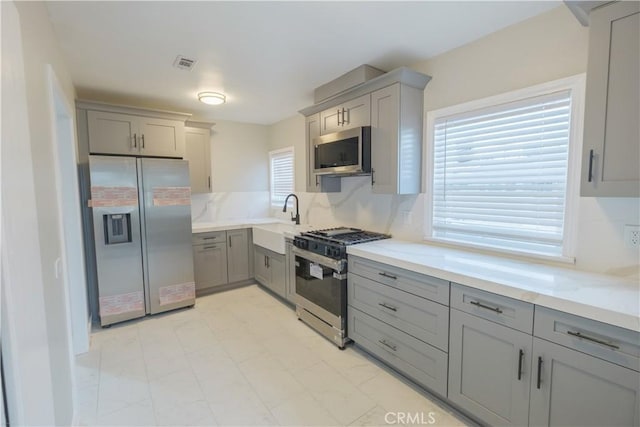 kitchen featuring appliances with stainless steel finishes, gray cabinets, sink, and backsplash