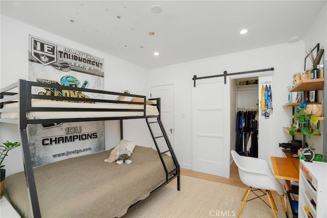 bedroom with a closet, crown molding, light hardwood / wood-style floors, and a barn door