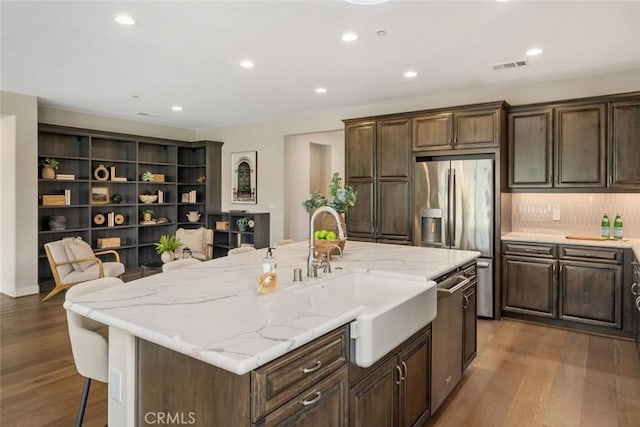 kitchen with stainless steel appliances, wood-type flooring, sink, and a center island with sink