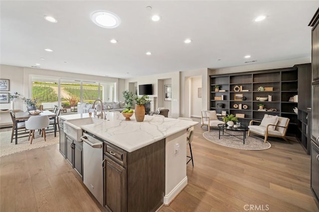 kitchen with sink, dishwasher, a kitchen island with sink, a kitchen breakfast bar, and light stone counters