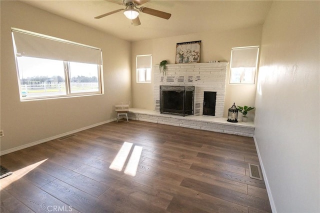 unfurnished living room with ceiling fan, dark hardwood / wood-style flooring, and a brick fireplace