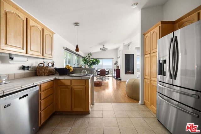 kitchen featuring pendant lighting, tile counters, light tile patterned floors, kitchen peninsula, and stainless steel appliances