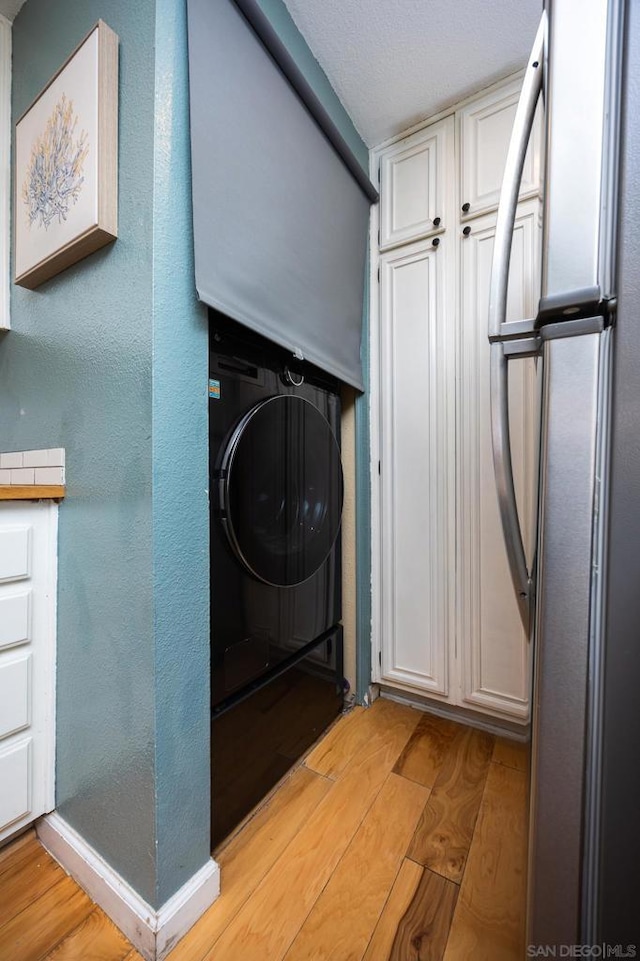 clothes washing area featuring cabinets, washer / dryer, a textured ceiling, and light wood-type flooring