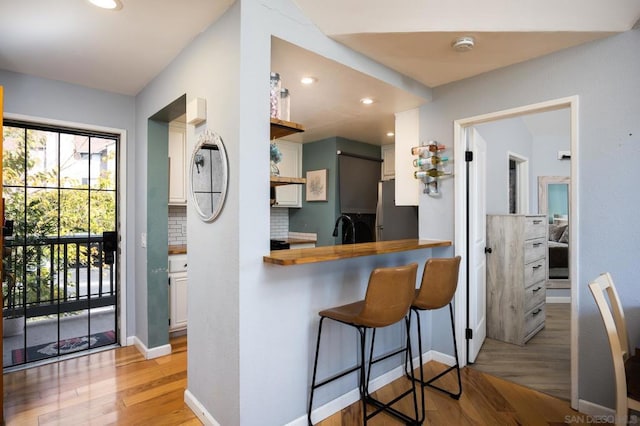 kitchen with sink, wooden counters, light wood-type flooring, stainless steel refrigerator, and decorative backsplash