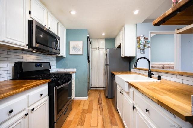 kitchen with sink, wooden counters, appliances with stainless steel finishes, white cabinetry, and light wood-type flooring