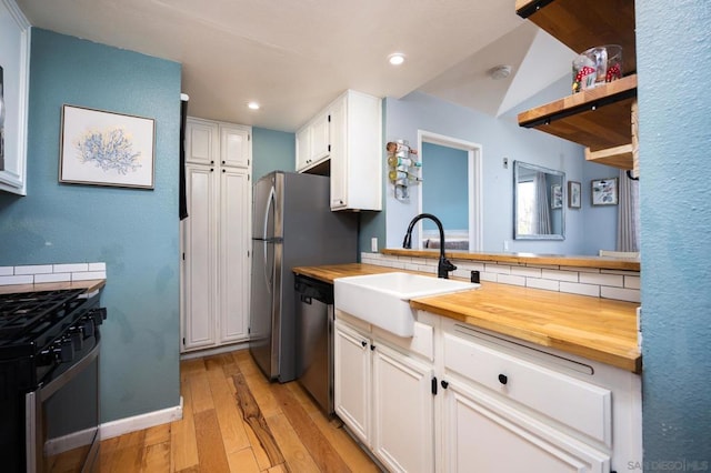 kitchen with stainless steel appliances, sink, white cabinets, and wood counters