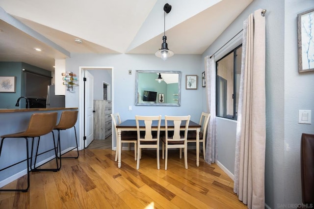 dining space with lofted ceiling, sink, and light wood-type flooring